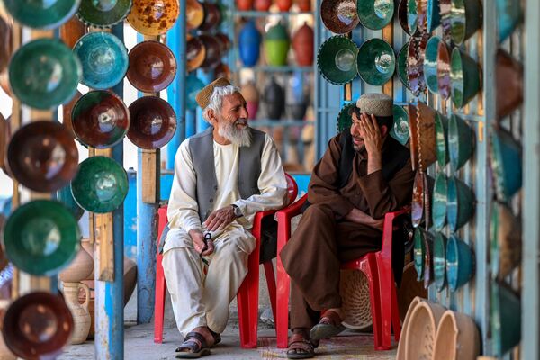 उत्तर-पश्चिमी काबुल प्रांत के एक बाज़ार में अफगान आगंतुक मिट्टी के कटोरे बेचने वाली दुकानों के सामने बैठे हैं। (Photo by Wakil Kohsar / AFP) - Sputnik भारत