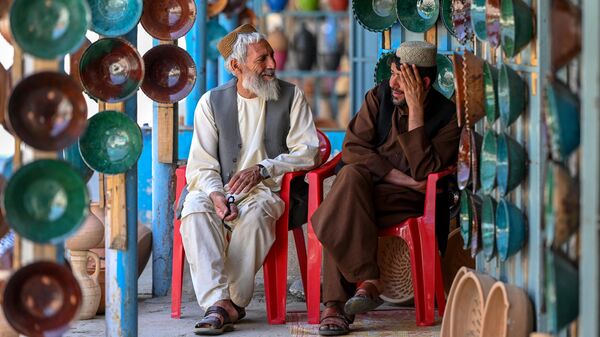 Afghan visitors sit in front of shops selling clay bowls at a market in Istalif district in the northwestern Kabul province on July 3, 2023. - Sputnik भारत