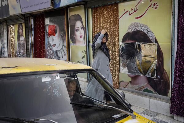 रविवार, 12 सितंबर, 2021 को काबुल, अफगानिस्तान में एक महिला खिड़की की सजावट के साथ ब्यूटी सैलून के पास से गुजरती है, जिसे विरूपित कर दिया गया है। (AP Photo/Bernat Armangue, File) - Sputnik भारत