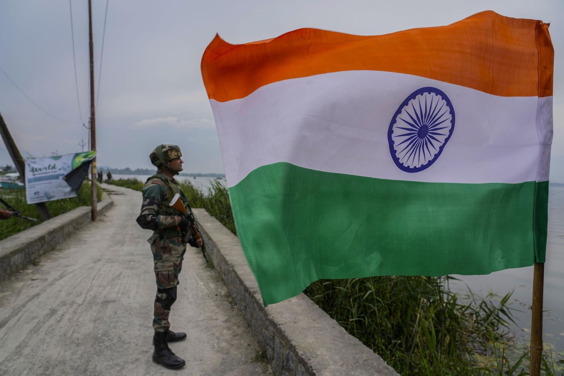 An Indian army soldier guard near an Indian flag as his colleagues remove weed from the polluted waters of the Dal Lake on World Environment Day in Srinagar, Indian controlled Kashmir, Monday, June 5, 2023.  - Sputnik भारत, 1920, 14.08.2023