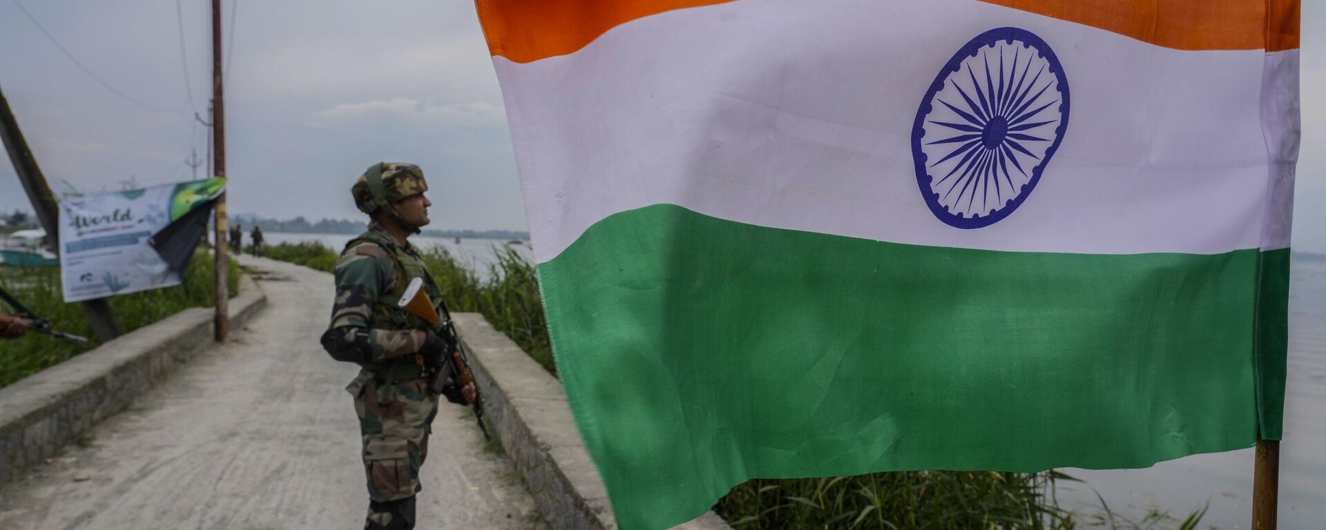 An Indian army soldier guard near an Indian flag as his colleagues remove weed from the polluted waters of the Dal Lake on World Environment Day in Srinagar, Indian controlled Kashmir, Monday, June 5, 2023.  - Sputnik भारत, 1920, 07.12.2023