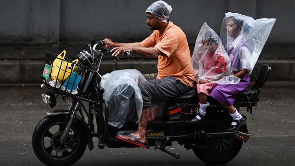A man rides a two-wheeler with two children covered with plastic sheets during a monsoon rainfall in Hyderabad on July 18, 2023. - Sputnik भारत