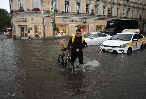 मास्को में भारी बारिश के कारण पानी में डूबी सड़क पर साइकिल चलाता एक व्यक्ति। मौसम वैज्ञानिकों ने दर्ज किया कि शहर के कुछ इलाकों में मासिक वर्षा की एक चौथाई से अधिक बारिश एक घंटे से भी कम समय में हुई। - Sputnik भारत