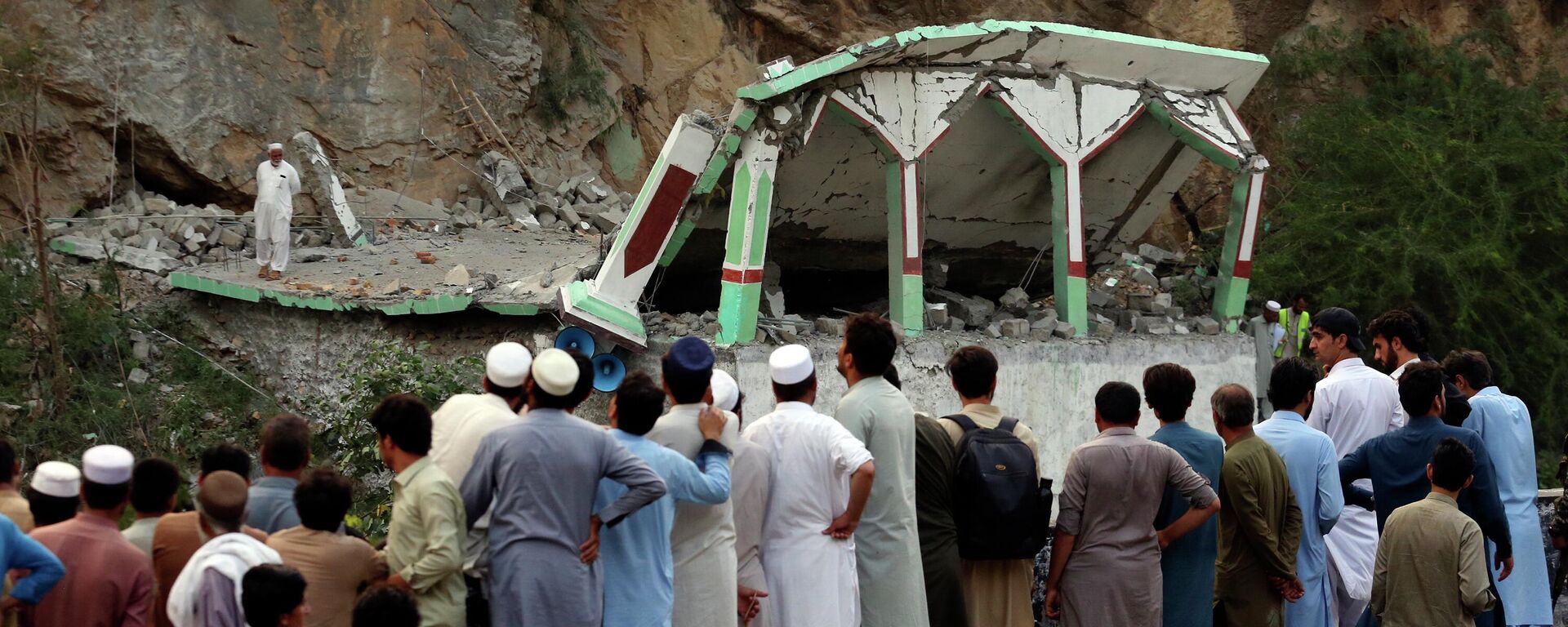 People Stand and watch the damaged mosque after a suicide bomber attack inside a roadside mosque in the Khyber district in Khyber Pakhtunkhwa province, of Pakistan, Tuesday,  July 25, 2023. A suicide bomber blew himself up inside a roadside mosque when a police officer tried to arrest him after a chase in northwestern Pakistan near the Afghan border on Tuesday, killing the officer, police said. - Sputnik भारत, 1920, 26.07.2023