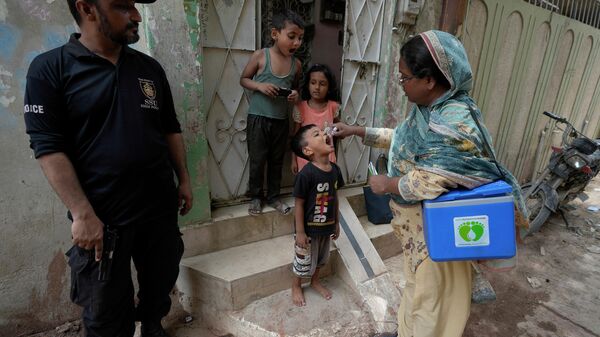 A police officer stands guard as a health worker administers a polio vaccine to a child at a neighbourhood of Karachi, Pakistan, Monday, June 19, 2023. - Sputnik भारत