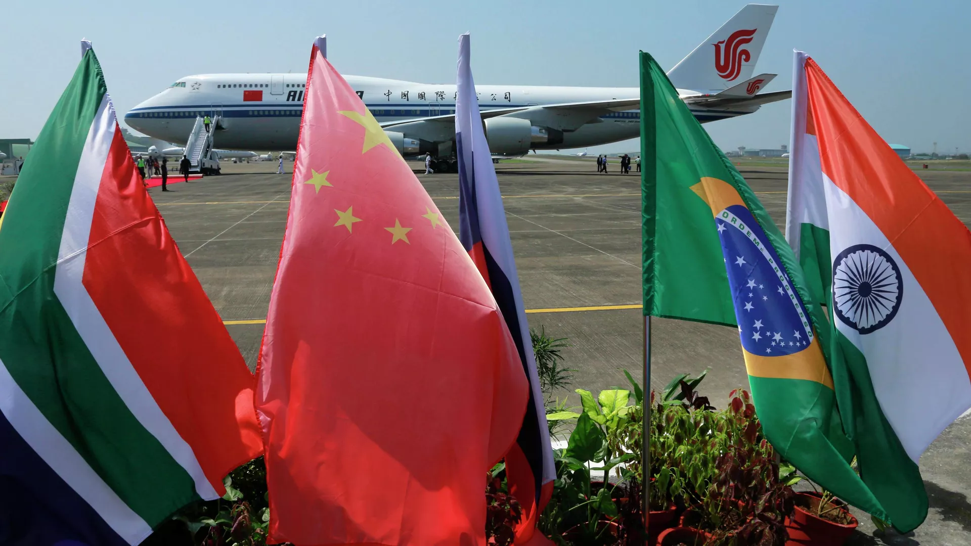 Flags of the five countries that make up BRICS fly in front of an Air China aircraft in which Chinese President Xi Jinping arrived to attend the BRICS summit in Goa, India, Saturday, Oct. 15 2016.