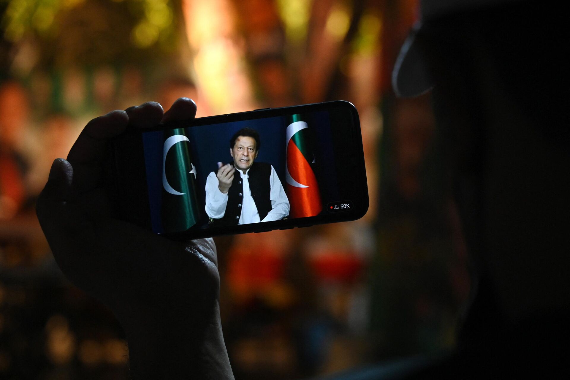An activist of Tehreek-e-Insaf (PTI) party listens to Pakistan's former Prime Minister Imran Khan's speech on a phone, in Zaman Park in Lahore on May 13, 2023. - Sputnik India, 1920, 08.08.2023