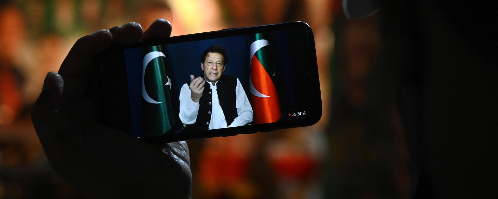 An activist of Tehreek-e-Insaf (PTI) party listens to Pakistan's former Prime Minister Imran Khan's speech on a phone, in Zaman Park in Lahore on May 13, 2023. - Sputnik भारत, 1920, 09.08.2023