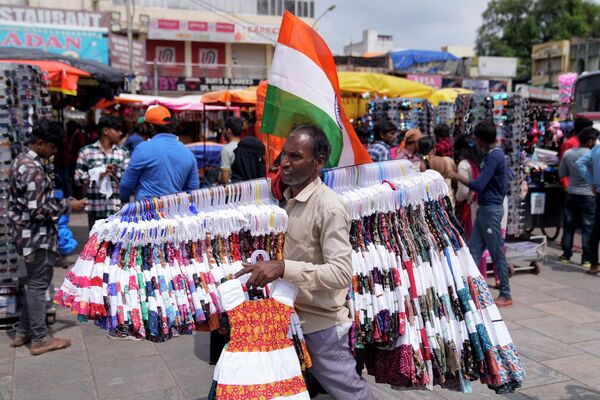 मंगलवार, 15 अगस्त, 2023 को हैदराबाद, भारत में सड़क कपड़ा विक्रेता ग्राहकों का इंतजार करते हुए अपने सामान के बीच भारतीय झंडा प्रदर्शित कर रहा है। (AP Photo/Mahesh Kumar A.) - Sputnik भारत