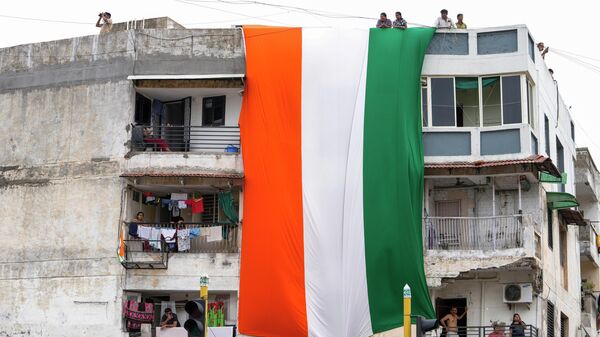 A huge tricolor hangs from a building as people march carrying Indian flags ahead of Independence Day in Ahmedabad, India, Sunday, Aug. 13, 2023. - Sputnik भारत