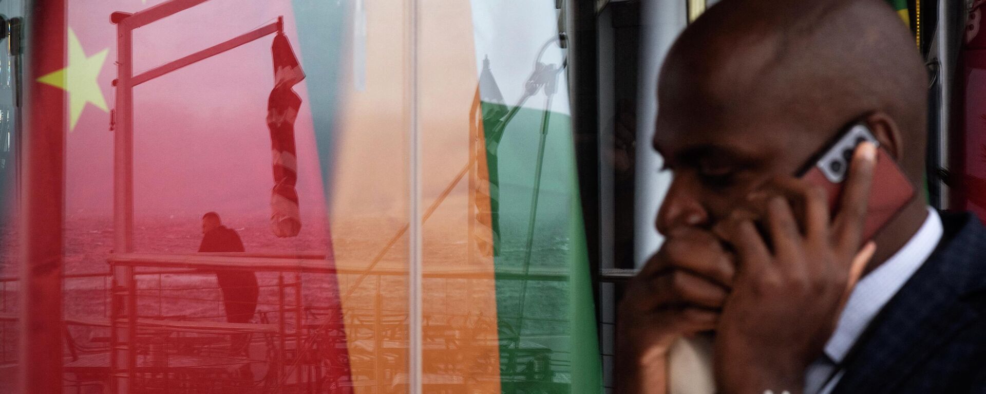 A man chats on a mobile phone as he walks past a reflection on a window of another man staring at the sea in front of the national flags of the BRICS (China, India, Russia, South Africa, Brazil) countries during the BRICS Foreign Ministers Meeting in Cape Town, on June 02, 2023. - Sputnik India, 1920, 20.08.2023