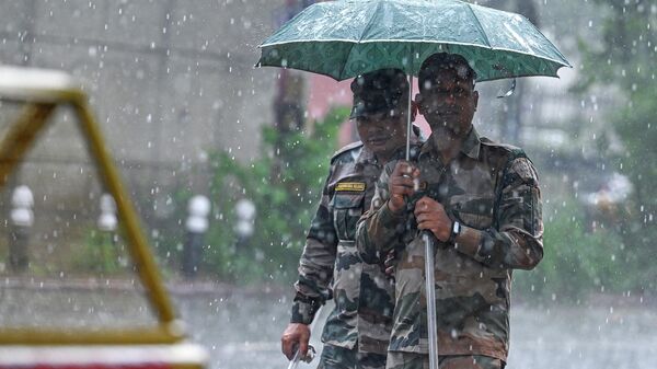 Security personnel use an umbrella to protect themselves amid heavy rainfall in New Delhi on July 18, 2023.  - Sputnik India