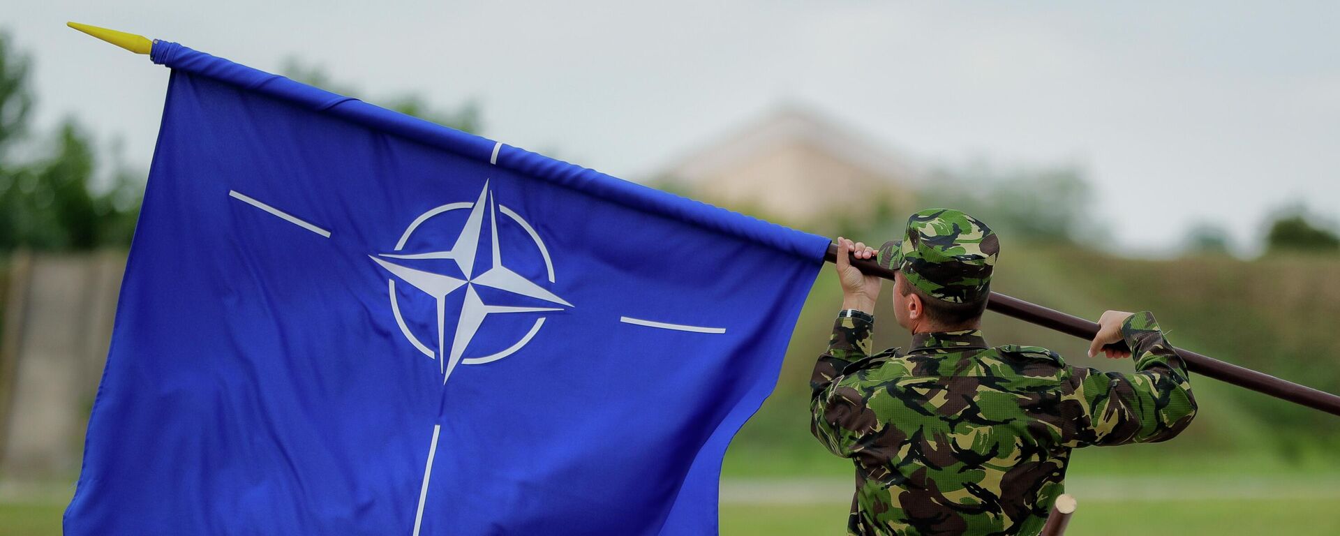 A Romanian serviceman furls the NATO flag. File photo - Sputnik भारत, 1920, 19.12.2025