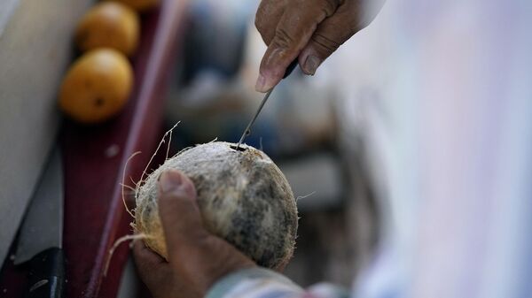 Andres Matamoros prepares a cold coconut for a customer while selling fresh fruit from his roadside stand Wednesday, June 28, 2023, in Houston. - Sputnik India