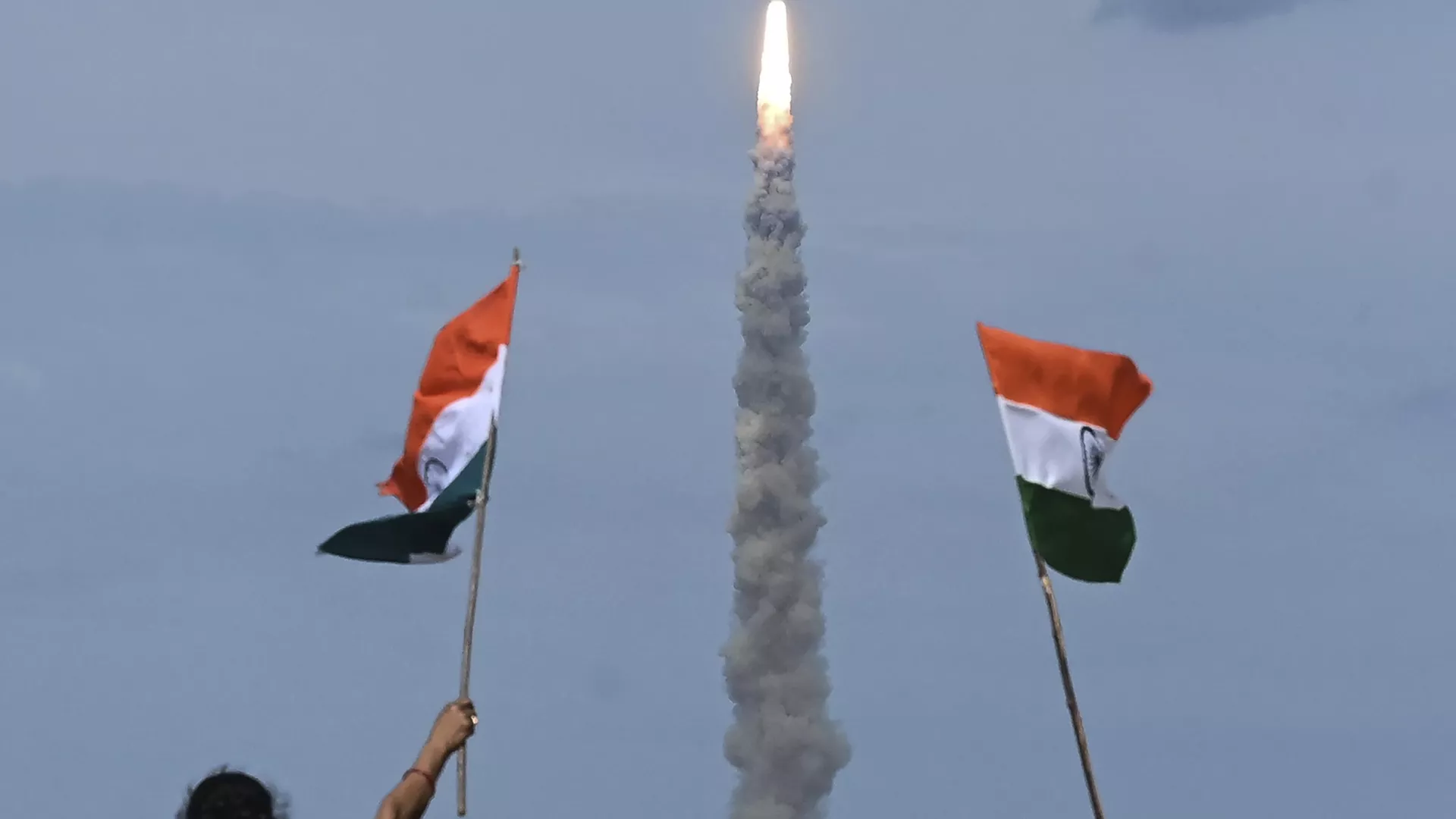 People wave Indian flags as an Indian Space Research Organisation (ISRO) rocket carrying the Chandrayaan-3 spacecraft lifts off from the Satish Dhawan Space Centre in Sriharikota, an island off the coast of southern Andhra Pradesh state on July 14, 2023. 