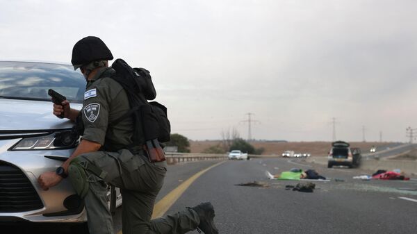 An Israeli soldier take cover behind a car as he looks toward bodies on a main road near the Gevim Kibbutz, close to the border with Gaza on October 7, 2023. - Sputnik भारत