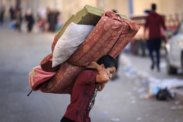 A boy carries a mattress as Palestinians with their belongings flee to safer areas in Gaza City after Israeli air strikes, on 13 October 2023. (MAHMUD HAMS / AFP) - Sputnik India