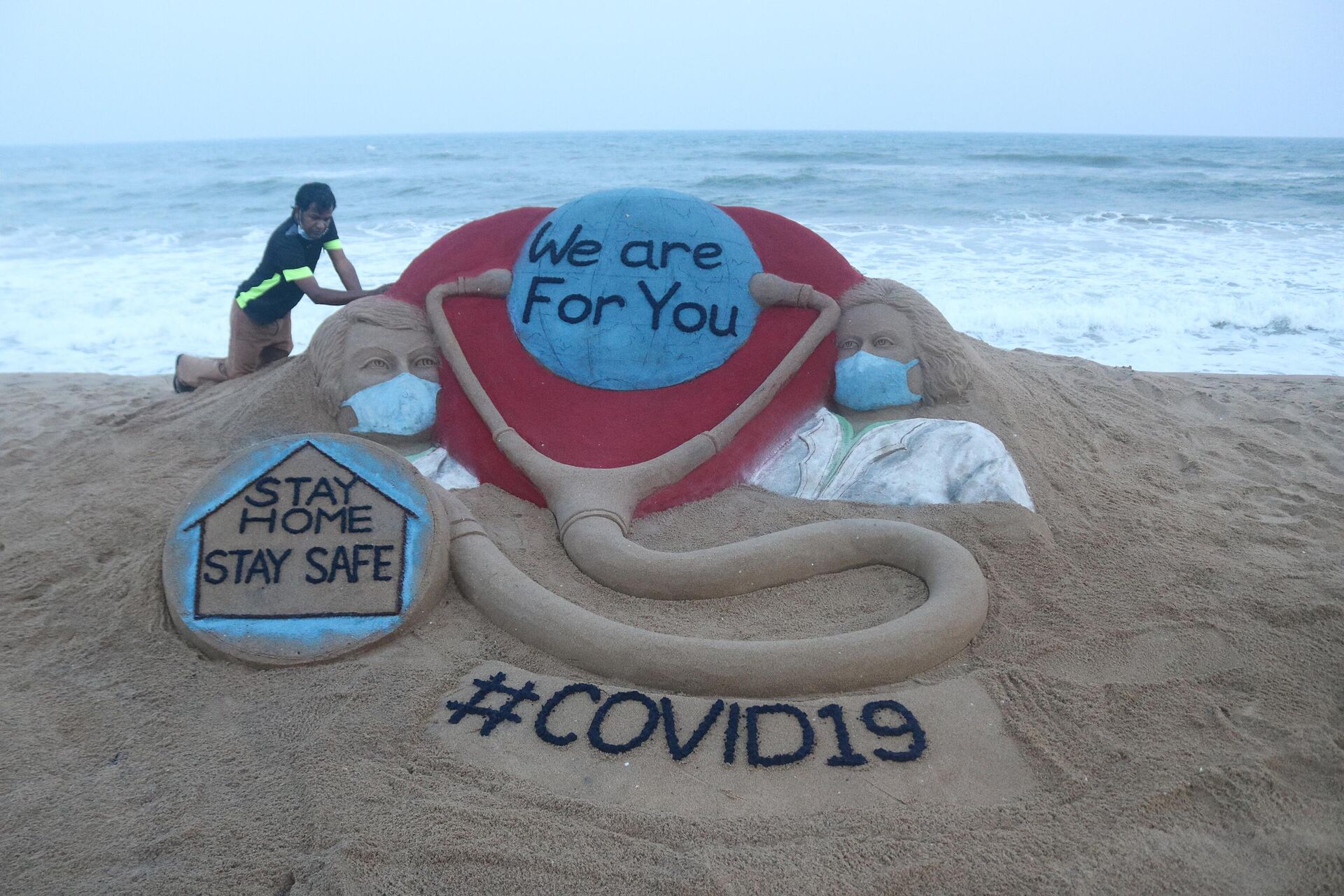 Indian artist Sudarsan Pattnaik puts some final touches as he makes a sand sculpture depicting doctors wearing protective facemasks with a message reading We are For You, Stay Home Stay Safe at Puri beach in Puri on April 3, 2020. - Sputnik India, 1920, 15.10.2023