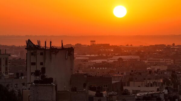 The sun rises behind a damaged building over the skyline of Khan Yunis in the southern Gaza Strip on October 19, 2023. - Sputnik भारत