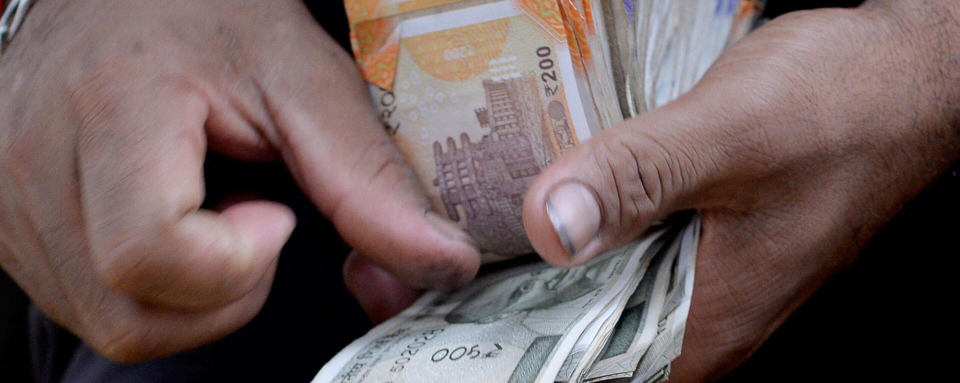 A fruit vendor counts a wad of Indian Rupee currency notes for payment at his roadside stall in Mumbai on July 19, 2022. The Indian rupee fell to more than 80 per US dollar for the first time on record on July 19, as the greenback extended its rally and foreign capital outflows intensified.  - Sputnik भारत, 1920, 30.01.2024