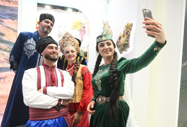 &#x27;क्रीमिया&#x27; स्टैंड के पास पारंपरिक  पोशाक पहने हुए प्रदर्शनी में भाग लेने वाले लोग खड़े हैं।  - Sputnik भारत
