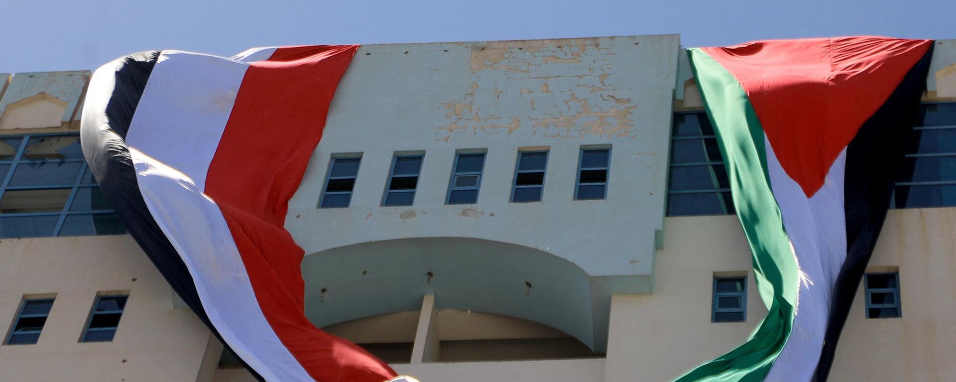 Two large flags, Palestine (L) and Yemen (R), are unfurled off the roof of a building in solidarity with the Palestinians of the West Bank and the Gaza Strip, on the sixth consecutive day of battles between Israel and the Hamas movement in the Gaza Strip enclave, on October 12, 2023, in the Houthi-controlled Yemeni capital Sanaa. - Sputnik भारत, 1920, 09.11.2023