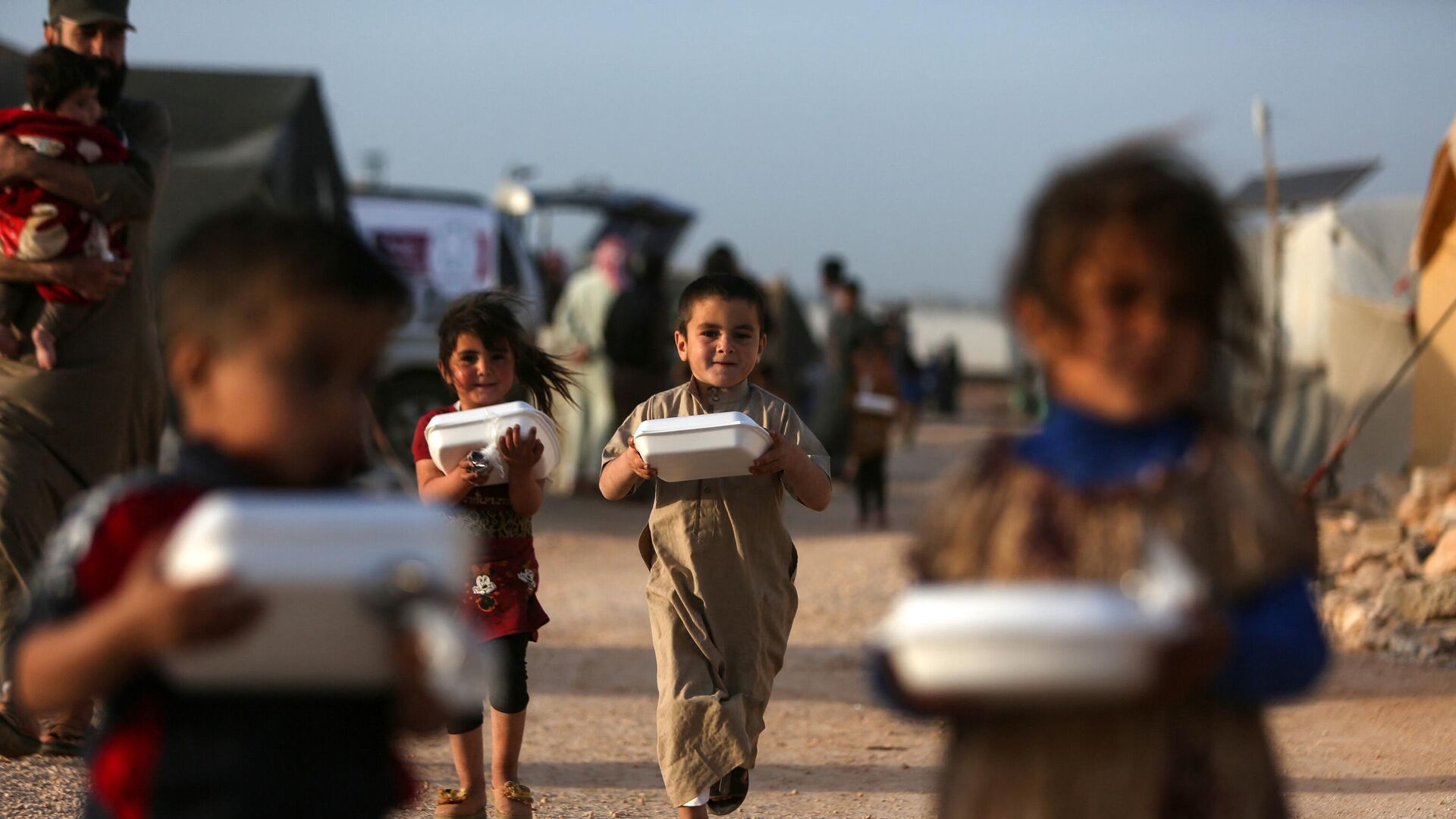 Displaced Syrian children return to their tents with boxes of food distributed by a local charity organisation, before the 'Iftar' meal during the Muslim holy month of Ramadan, at a camp for displaced people on the outskirts of the rebel-held town of Dana, east of the Turkish-Syrian border in the northwestern Idlib province, on April 3, 2022. - Sputnik India, 1920, 10.11.2023