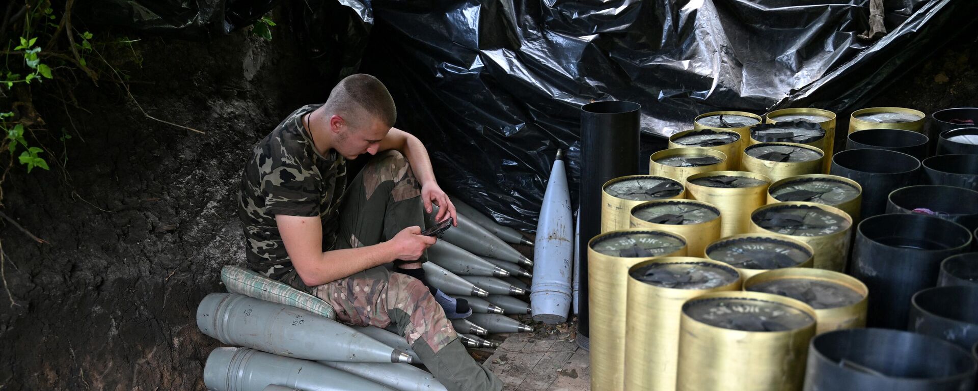 A Ukrainian artilleryman checks his mobile phone next to shells and the cases of propellant charges as he gets a rest at a position near Avdeyevka in the Donetsk region on June 23, 2023. - Sputnik भारत, 1920, 21.11.2023