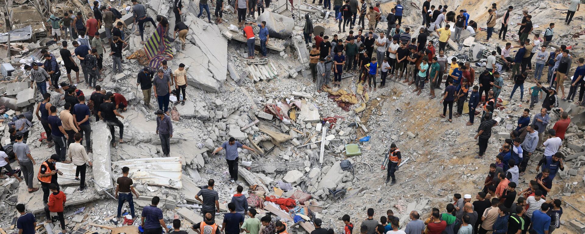 Civilians and rescuers look for survivors amid the rubble of a destroyed building following an Israeli bombardment in Khan Yunis in the southern Gaza Strip, amid the ongoing battles between Israel and the Palestinian militant group Hamas.  - Sputnik भारत, 1920, 23.11.2023