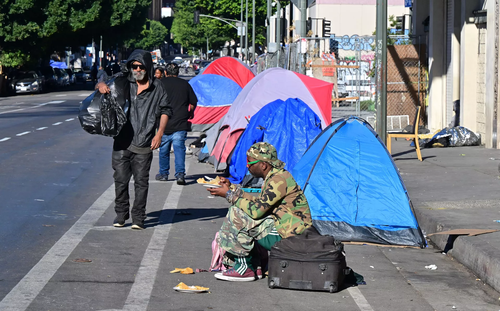 A homeless man sits on a suitcase on the side of a street lined with tents housing the homeless in Downtown Los Angeles on November 22, 2023. A homeless man sits on a suitcase on the side of a street lined with tents housing the homeless in Downtown Los Angeles on November 22, 2023. - Sputnik India, 1920, 04.01.2024