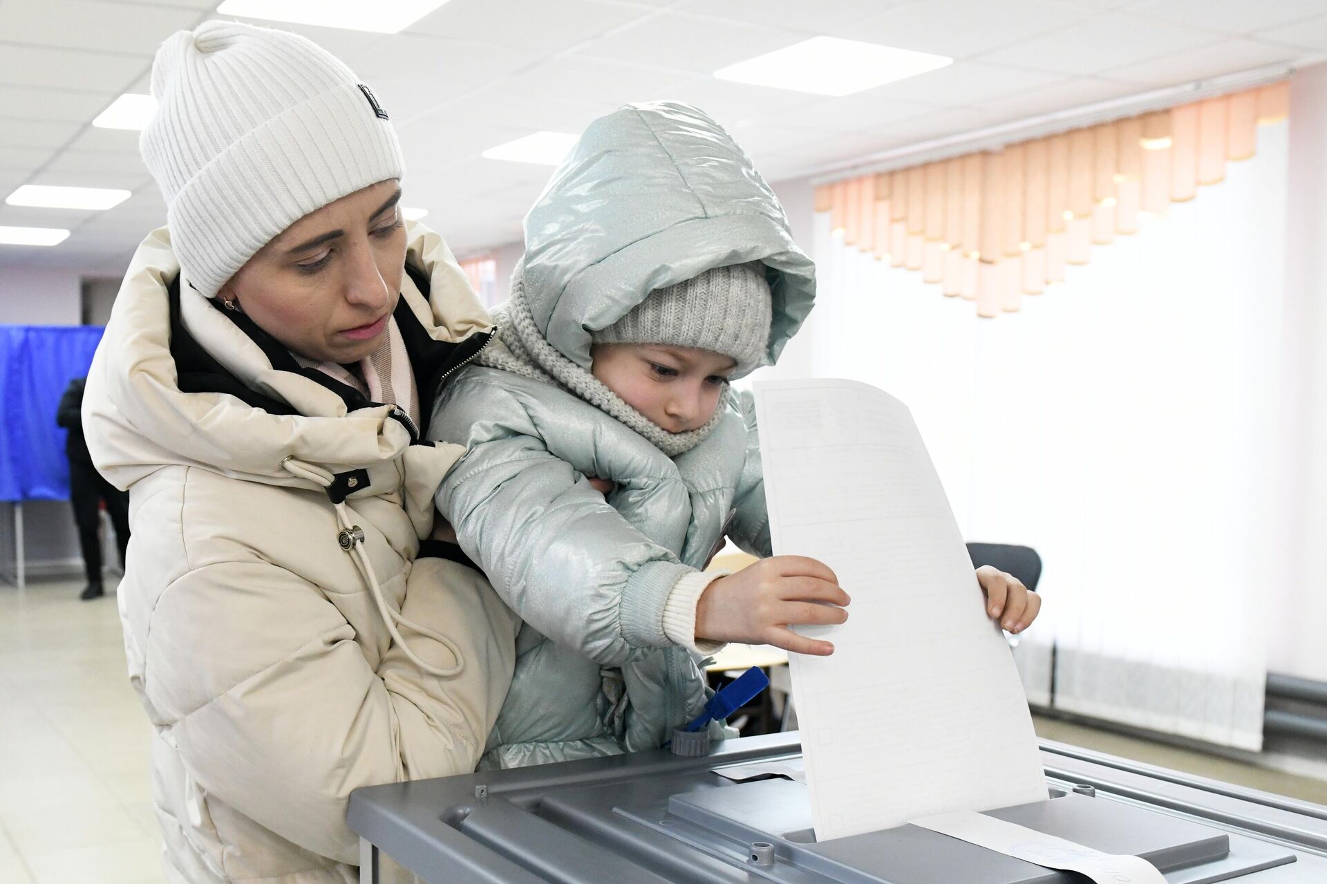 A woman with a child casts her ballot at a polling station during the presidential election in Kirovskoye - Sputnik India, 1920, 26.03.2024