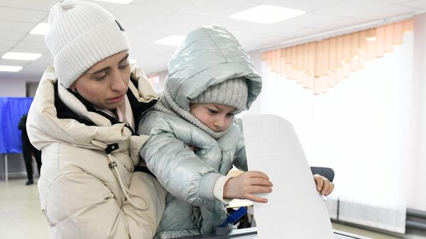 A woman with a child casts her ballot at a polling station during the presidential election in Kirovskoye - Sputnik India
