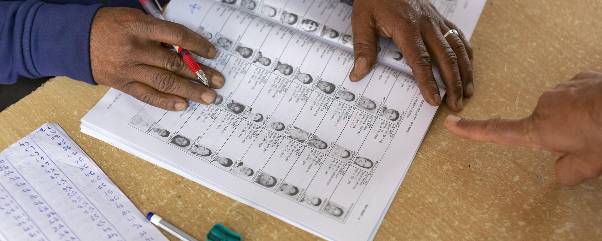 An election official checks a voters record in a register before allowing him to cast his ballot in a bypoll for an assembly seat in Dharmsala, India, Monday, Oct. 21, 2019. - Sputnik India, 1920, 16.03.2024
