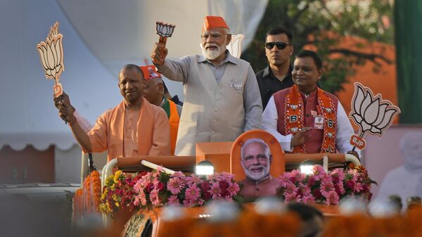 Indian Prime Minister Narendra Modi, center, in a saffron cap, and Chief Minister of Uttar Pradesh Yogi Adityanath, left, in saffron robes, ride in an open vehicle as they campaign for Bharatiya Janata Party (BJP) for the upcoming parliamentary elections in Ghaziabad, India, Saturday, April 6, 2024.  - Sputnik भारत