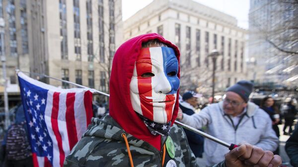 A man, wearing a patriotic colored Guy Fawkes mask and holding an American flag, joins a small group of protesters near the Manhattan District Attorney's office, Tuesday, March 21, 2023, in New York, in an anticipation of former President Donald Trump's possible indictment. A New York grand jury investigating Trump over a hush money payment to a porn star appears poised to complete its work soon as law enforcement officials make preparations for possible unrest in the event of an indictment. (AP Photo/Eduardo Munoz Alvarez) - Sputnik India