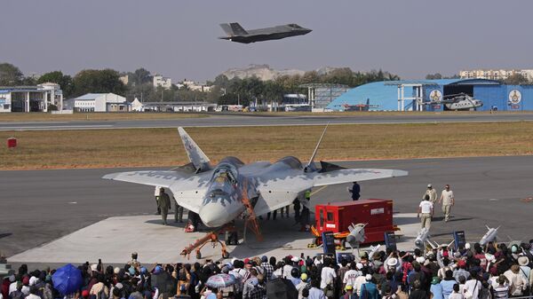 Visitors watch as U.S. Air Force fighter aircraft F-35 flies over Russia's Su-57 fighter aircraft, parked at the static display area, on the fourth day of the Aero India 2025, a biennial event, at Yelahanka air base in Bengaluru, India, Thursday, Feb. 13, 2025. (AP Photo/Aijaz Rahi) - Sputnik India