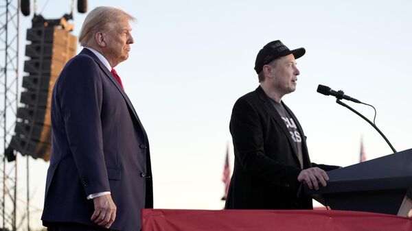 Tesla and SpaceX CEO Elon Musk speaks as Donald Trump listens at a campaign event at the Butler Farm Show, Saturday, Oct. 5, 2024. - Sputnik भारत