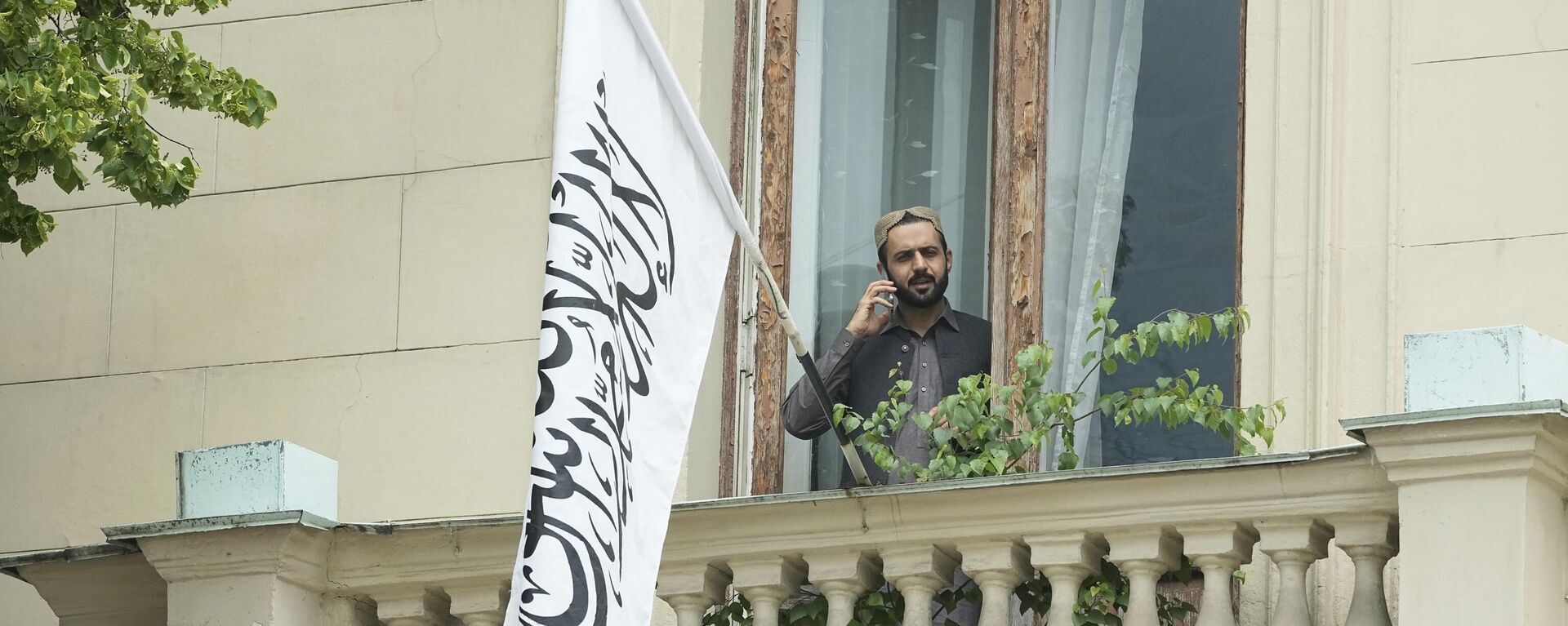 A man talks by a phone while standing on a balcony of the Afghan Embassy in Moscow, Russia, Friday, July 4, 2025, where the flag of the Islamic Emirate of Afghanistan was raised after Russia recognized the Taliban government in Afghanistan. - Sputnik India, 1920, 04.07.2025
