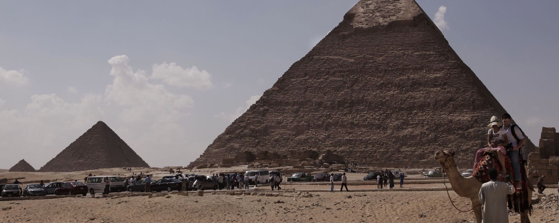 Tourists ride a camel as they visit the historical site of the Giza Pyramids, in front of the Khafre pyramid, right, near Cairo, Egypt. File photo. - Sputnik भारत, 1920, 01.08.2025