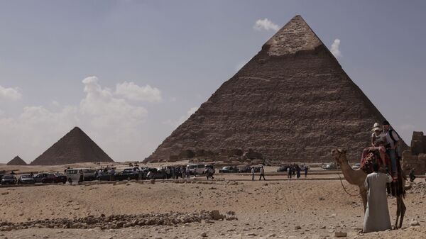 Tourists ride a camel as they visit the historical site of the Giza Pyramids, in front of the Khafre pyramid, right, near Cairo, Egypt. File photo. - Sputnik भारत