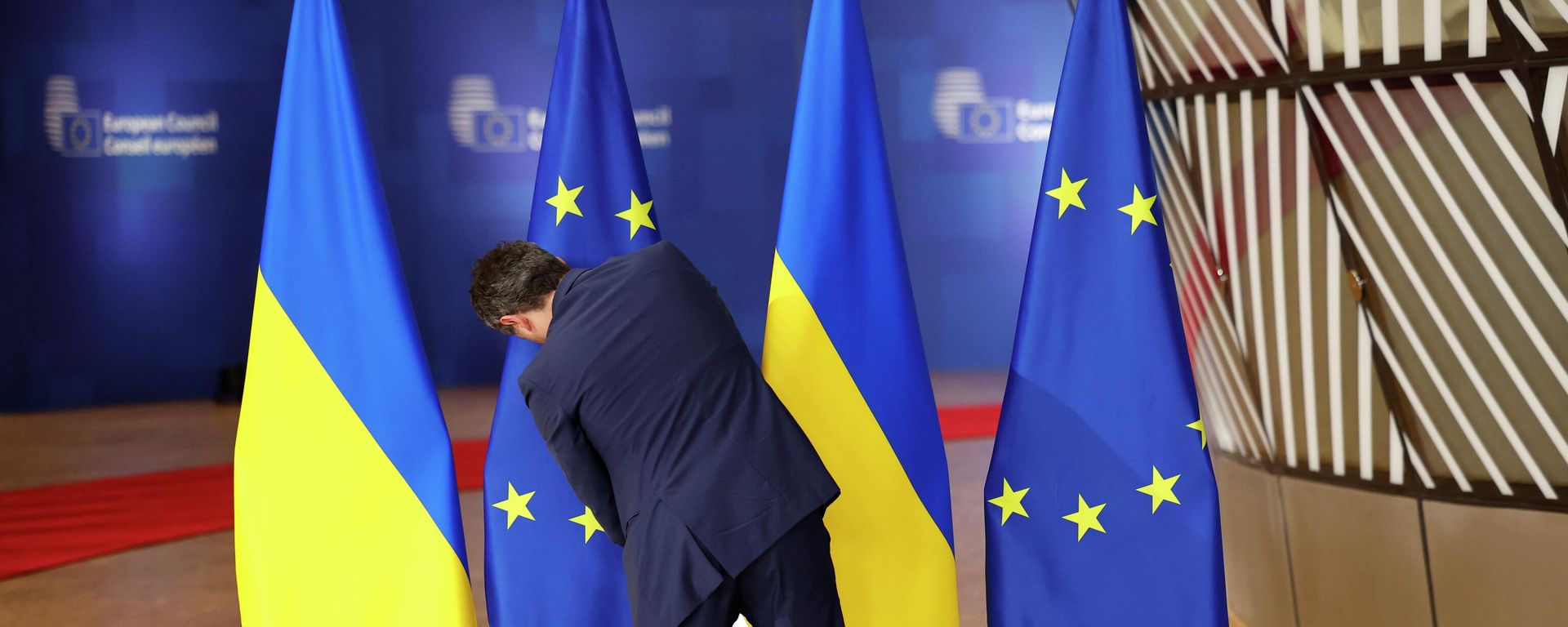 A member of protocol adjusts the EU and Ukrainian flags prior to arrivals for an EU summit at the European Council building in Brussels, Dec. 19, 2024. - Sputnik भारत, 1920, 21.08.2026