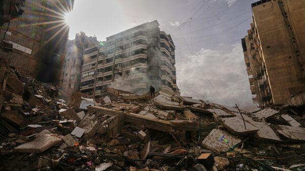A man stands atop the rubble as smoke rises from a building destroyed in an Israeli airstrike in Dahiyeh, Beirut's southern suburbs, Lebanon, Saturday, March 14, 2026. (AP Photo/Hassan Ammar) - Sputnik भारत