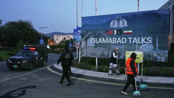 A worker cleans the street as police officers walks towards their vehicle outside a media center close to Serena Hotel, the venue for the U.S. Iran officials meeting, in Islamabad, Pakistan, Sunday, April 12, 2026. - Sputnik भारत