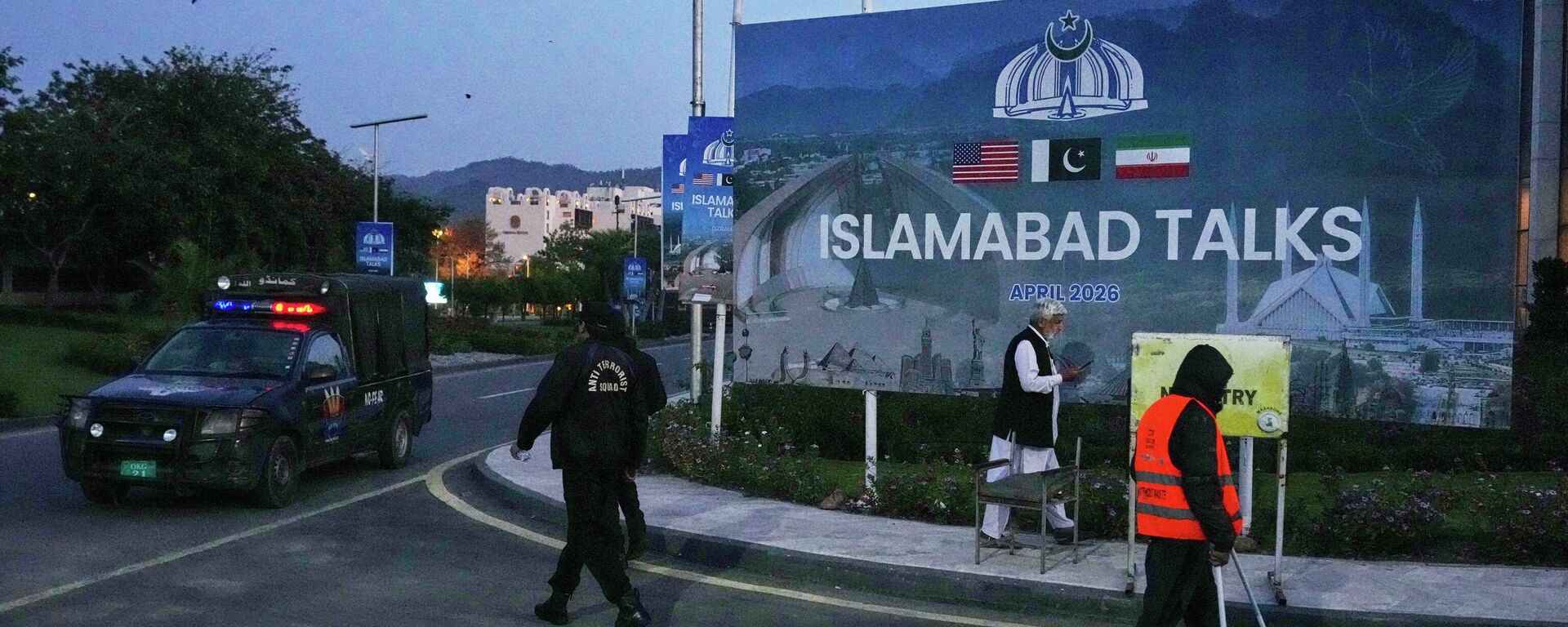 A worker cleans the street as police officers walks towards their vehicle outside a media center close to Serena Hotel, the venue for the U.S. Iran officials meeting, in Islamabad, Pakistan, Sunday, April 12, 2026. - Sputnik भारत, 1920, 20.04.2026
