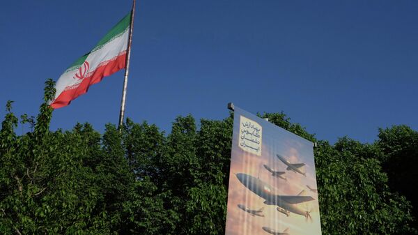 A banner shows a graphic depicting Iranian-built drones with a sign in Farsi that reads: Arash drone is the nightmare for Iran's enemies, as an Iranian flag waves at left, in Tehran, Iran, Tuesday, April 21, 2026.  - Sputnik भारत