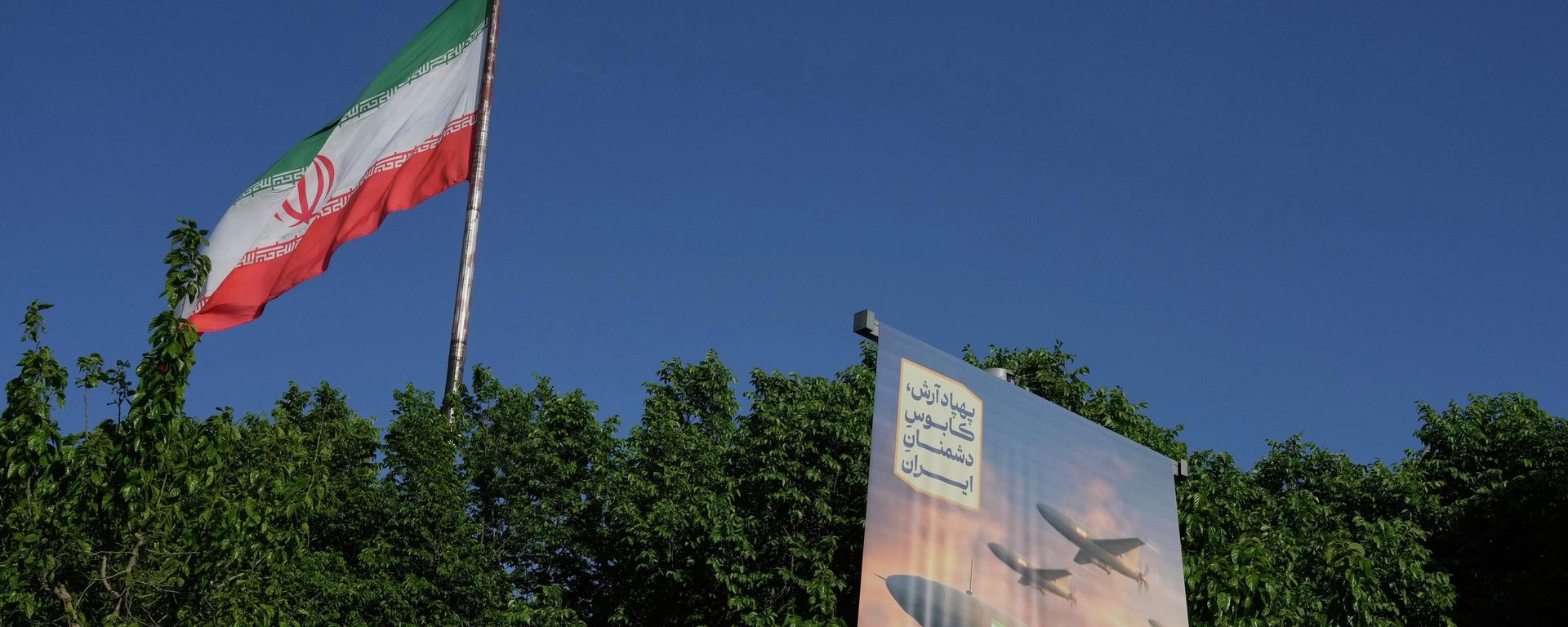 A banner shows a graphic depicting Iranian-built drones with a sign in Farsi that reads: Arash drone is the nightmare for Iran's enemies, as an Iranian flag waves at left, in Tehran, Iran, Tuesday, April 21, 2026.  - Sputnik भारत, 1920, 08.07.2026