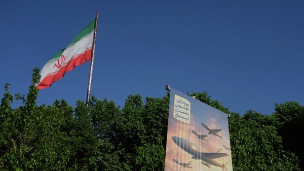 A banner shows a graphic depicting Iranian-built drones with a sign in Farsi that reads: Arash drone is the nightmare for Iran's enemies, as an Iranian flag waves at left, in Tehran, Iran, Tuesday, April 21, 2026.  - Sputnik भारत