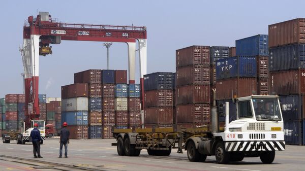 Workers watch as a truck passes by stacks of shipping containers at a port in Yingkou in northeastern China's Liaoning Province.  - Sputnik भारत