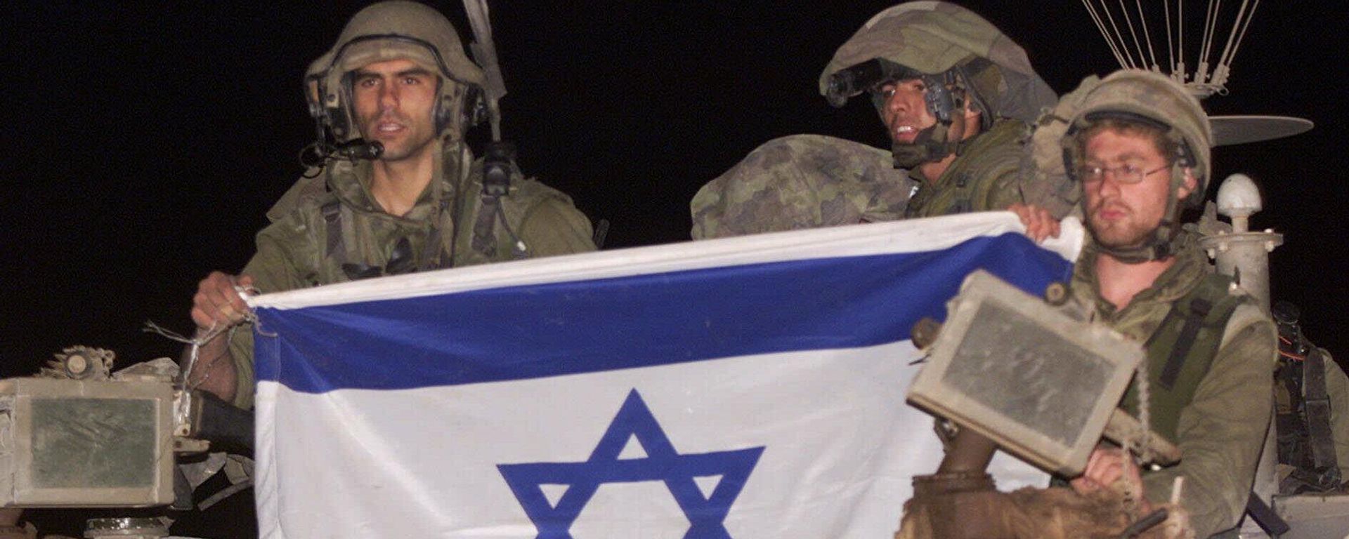 Israeli soldiers ride atop their armored vehicle holding an Israeli flag as they withdraw from south Lebanon into Israel, at the Israeli-Lebanese border near Metulla, early Wednesday, May 24, 2000.  - Sputnik भारत, 1920, 25.06.2026